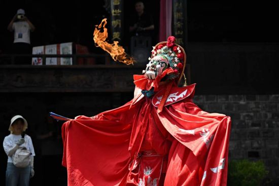 6月14日，游客在万灵古镇观看变脸吐火表演。中新社记者